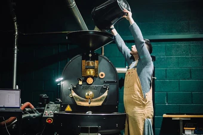 A roaster at Craft Decaf tipping green coffee into a Probat roasting machine