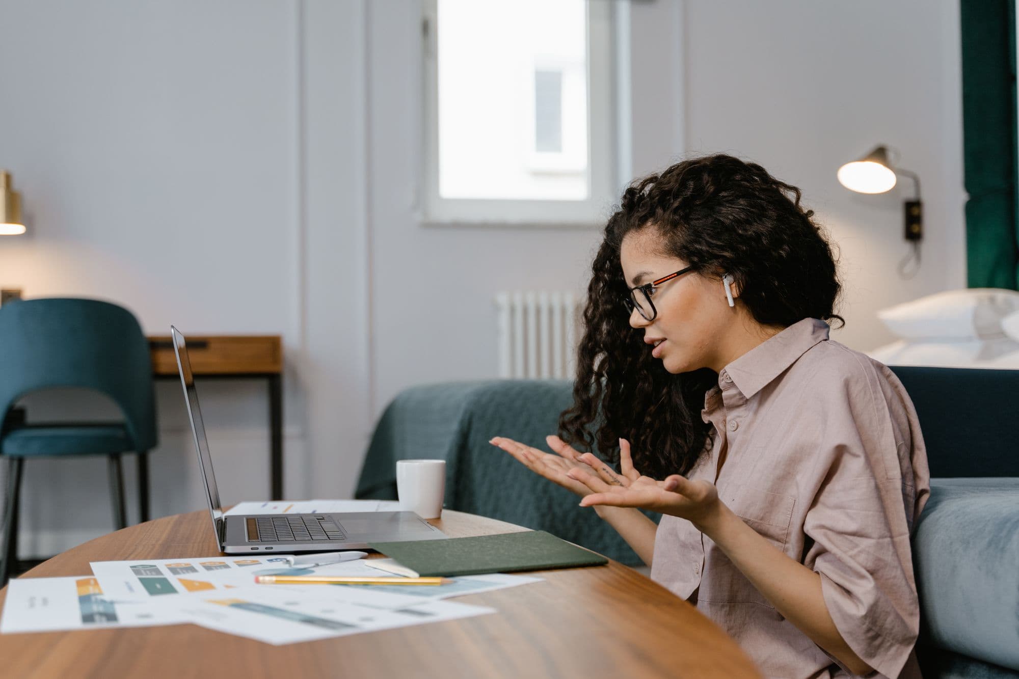 A woman on a video call with her team from her living room, papers spread across the table