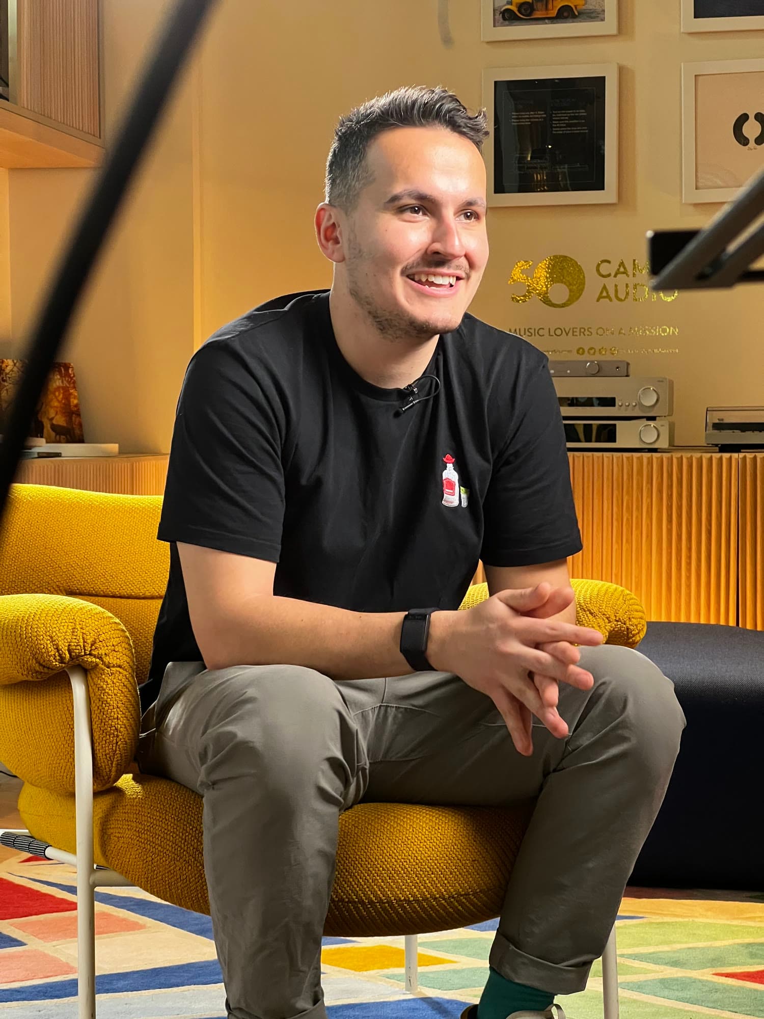Ken, smiling and sitting forward in a yellow armchair during an interview